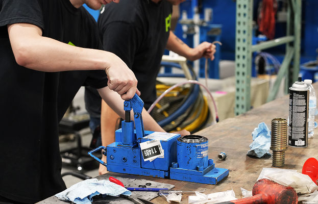 PJi technicians operating hydraulic equipment on a workbench during an aviation maintenance process in the workshop.