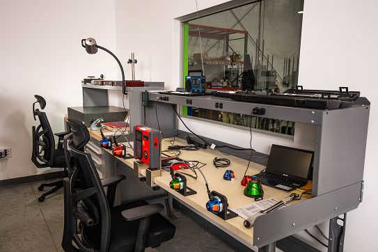 Workstation with calibration and testing equipment, laptops, and tools arranged on a long bench in a lab setting.