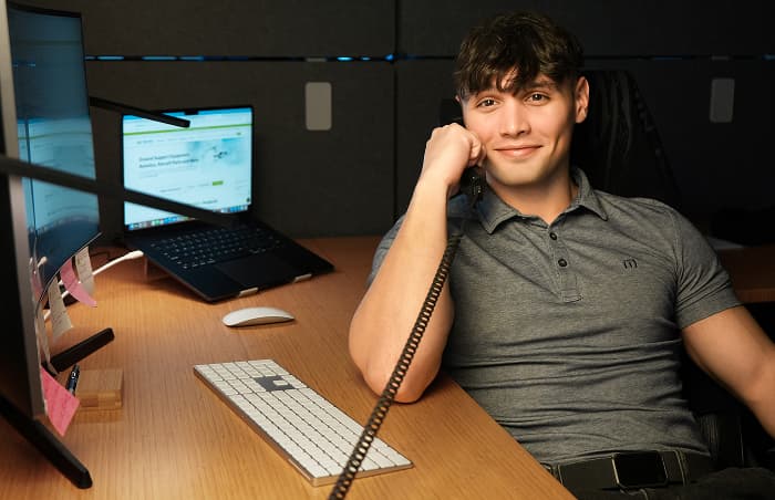 Smiling office worker on the phone at his desk with dual monitors displaying PJi financing page