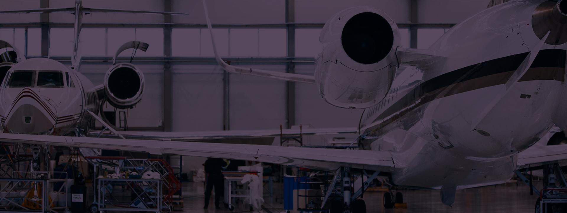 A spacious aircraft maintenance hangar with multiple private jets undergoing servicing, with tools, equipment, and technicians working in the background.