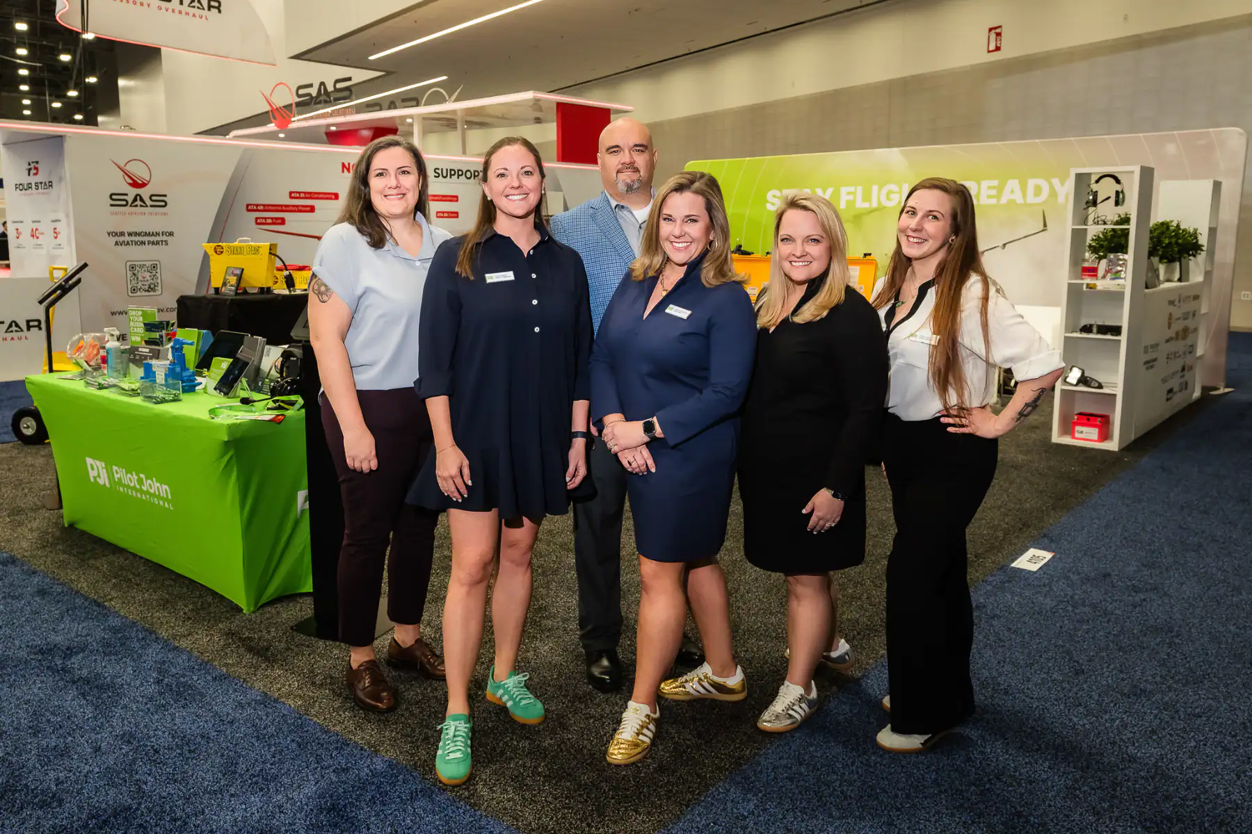 PJi team standing together at an aviation industry event booth with Pilot John International display table and signage in the background.