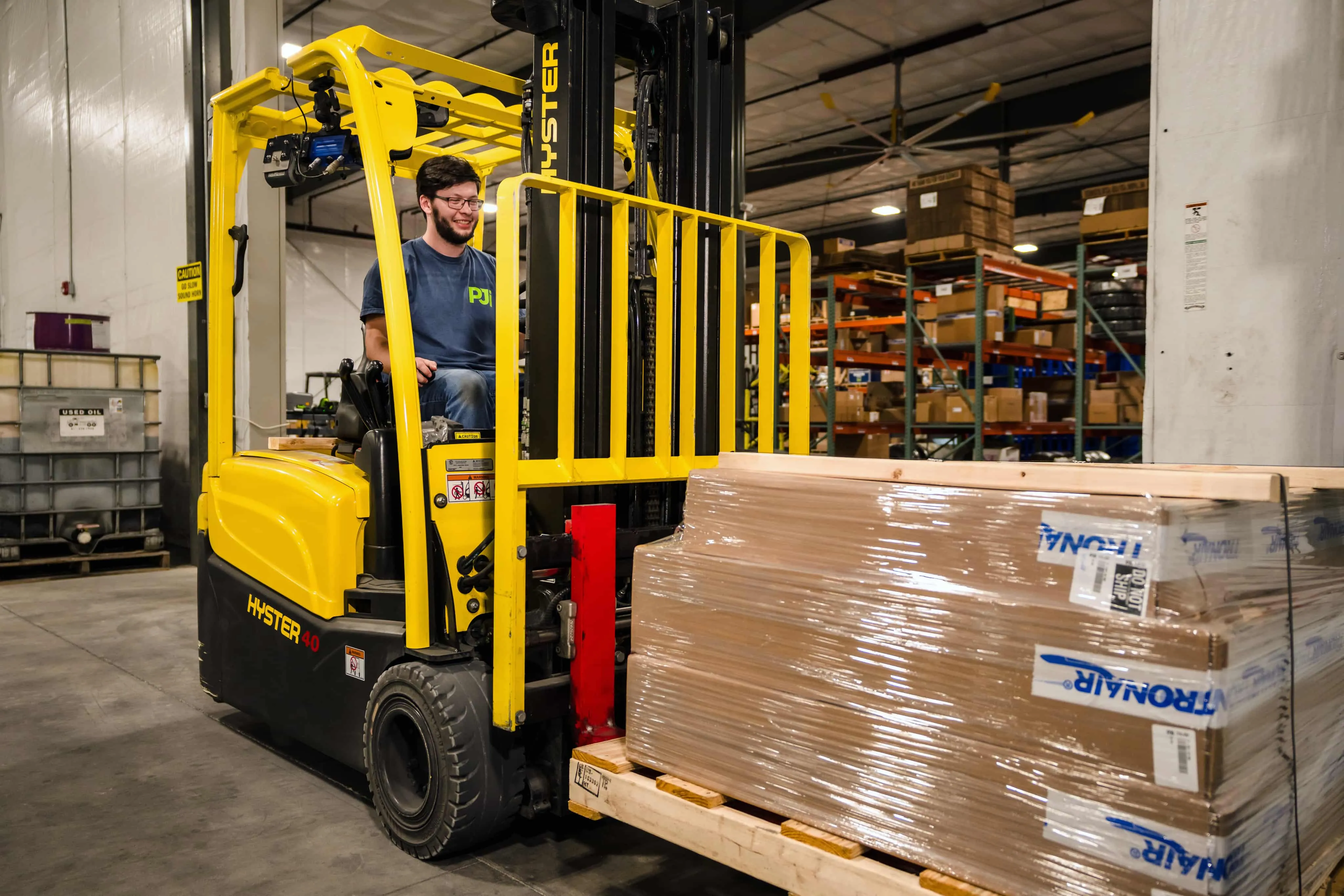 PJi warehouse employee operating a yellow Hyster forklift to move a pallet of packaged aviation equipment.