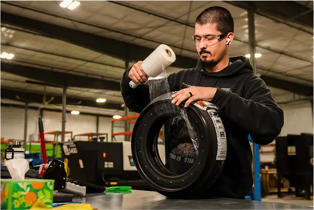 PJi employee wrapping protective plastic around an aircraft tire at a workbench in the warehouse.
