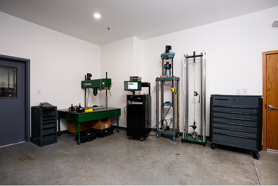 Calibration lab with hydraulic and mechanical testing equipment, workbench, and tool storage cabinets.