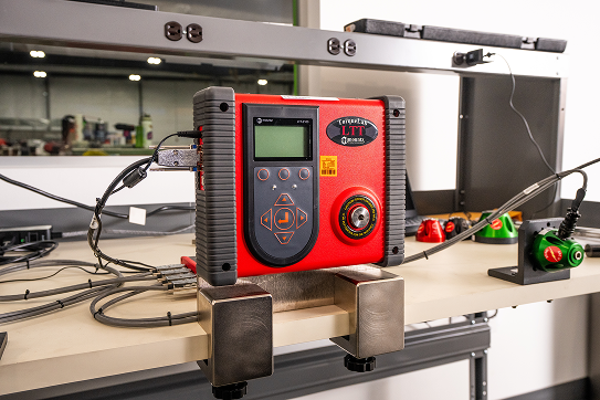 Red digital pressure calibrator mounted on a workbench with connected cables and fittings in a lab environment.