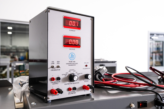 Electrical calibration device with red digital displays for current and voltage on a workbench.