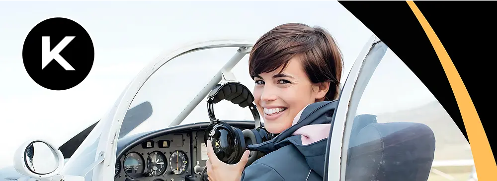 Smiling female pilot sitting in a cockpit holding a Kore Aviation headset, with the Kore Aviation logo in the top left corner.
