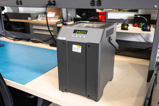 Laboratory dry block temperature calibrator displaying 25.00Â°C on a workbench.